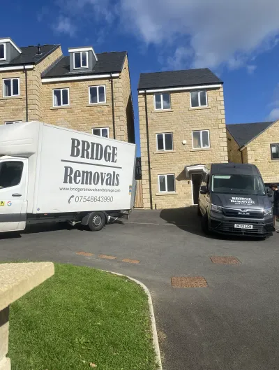 Two Bridge Removals vans outside sunlit new-build stone townhouses