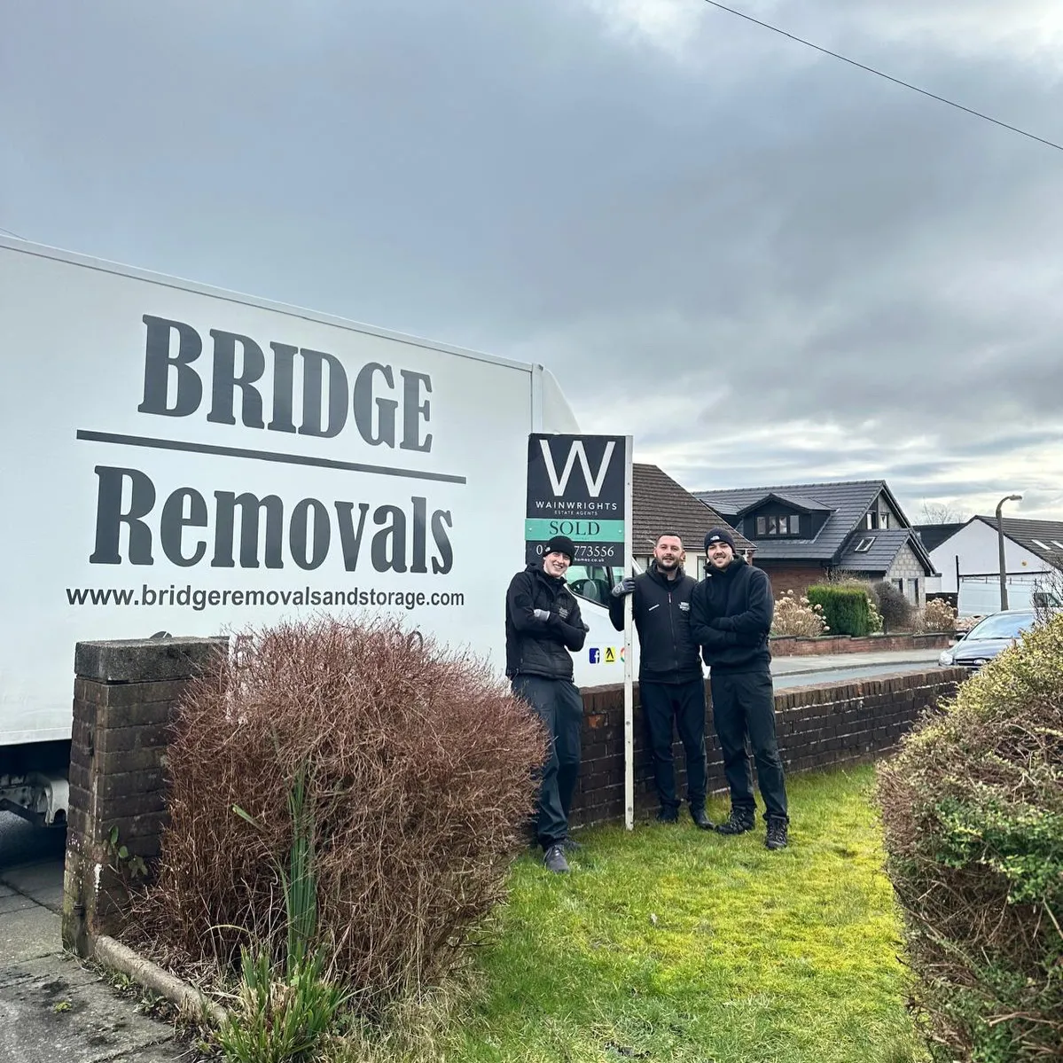 Three Bridge Removals crew members beside an estate agent's SOLD board after a completed move. Three Bridge Removals crew members beside an estate agent's SOLD board after a completed move.